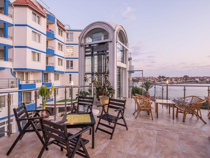 Terrazza con sedie e tavoli davanti a un moderno edificio dell'hotel con vista sull'acqua.