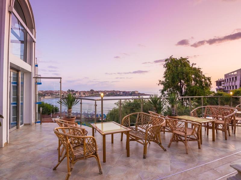 Terrazza con sedie in vimini e tavoli con vista sul mare al tramonto.