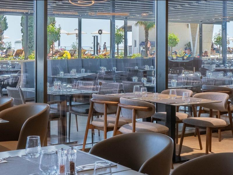 Ristorante moderno e elegante con grandi finestre e mobili in legno che si affacciano su una terrazza.