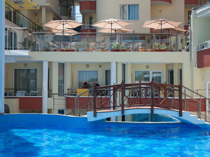 Una piscina con un piccolo ponte e ombrelloni davanti a un edificio dell'hotel.