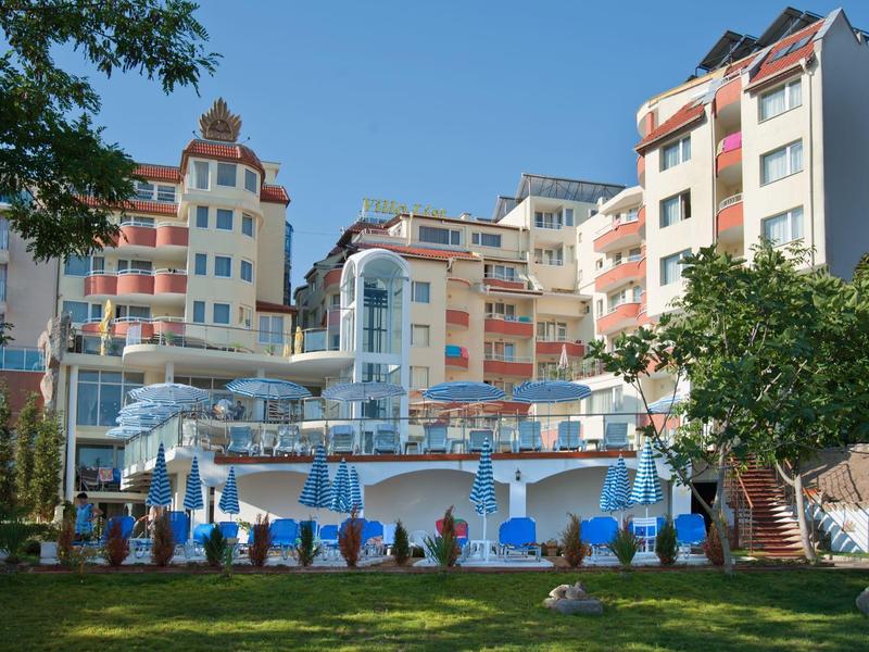 Hotel con piscina, ombrelloni e lettini davanti a edifici pluripiano in una giornata di sole.