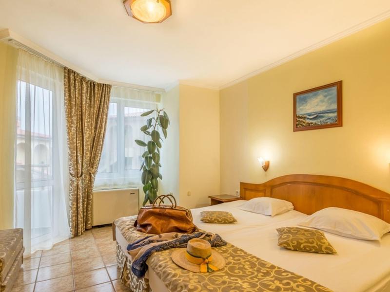 Camera d'hotel luminosa con due letti singoli, finestra con tende e pareti gialle.