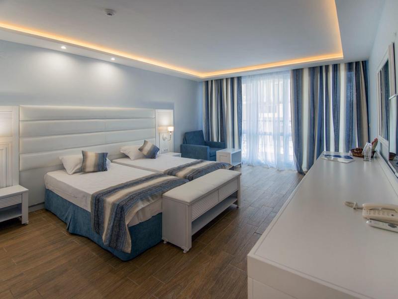 Camera d'hotel moderna con letto matrimoniale, zona salotto e grande finestra con tende.