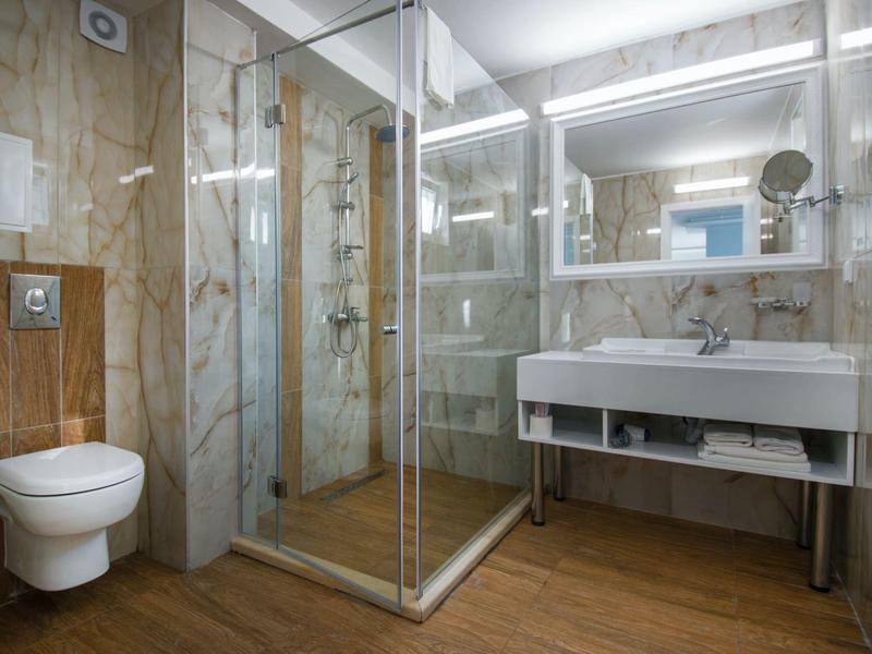 Bagno moderno con doccia in vetro, WC sospeso e grande specchio sopra il lavabo.
