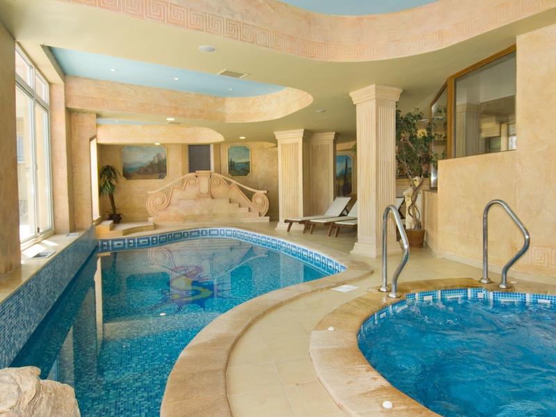 Elegante piscina interna con vasca idromassaggio e grandi finestre in tonalità beige calde.