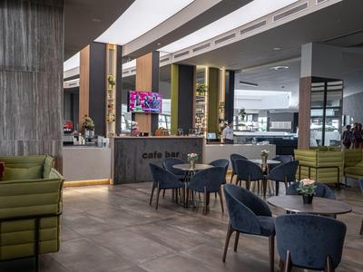 Moderne hotel lounge met blauwe stoelen, groene bank en goed verlichte cafebar.