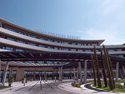 Modern gebogen resortgebouw met buitenpergola en palmbomen onder blauwe lucht.