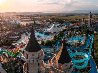 Brede luchtfoto van een groot pretpark met glijbanen en kasteeltorens bij zonsondergang.