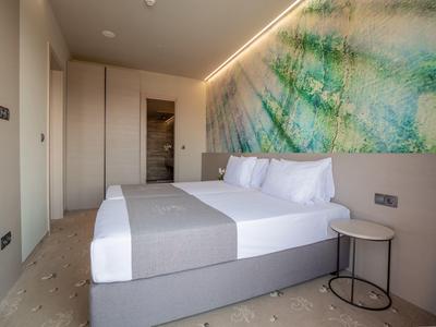 Moderne hotelkamer met tweepersoonsbed, licht houten vloer, abstracte muurkunst en rond bijzettafeltje.