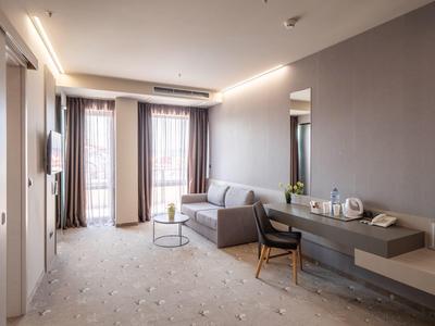 Moderne hotelkamer met bank, bureau, stoel en grote ramen met gordijnen.