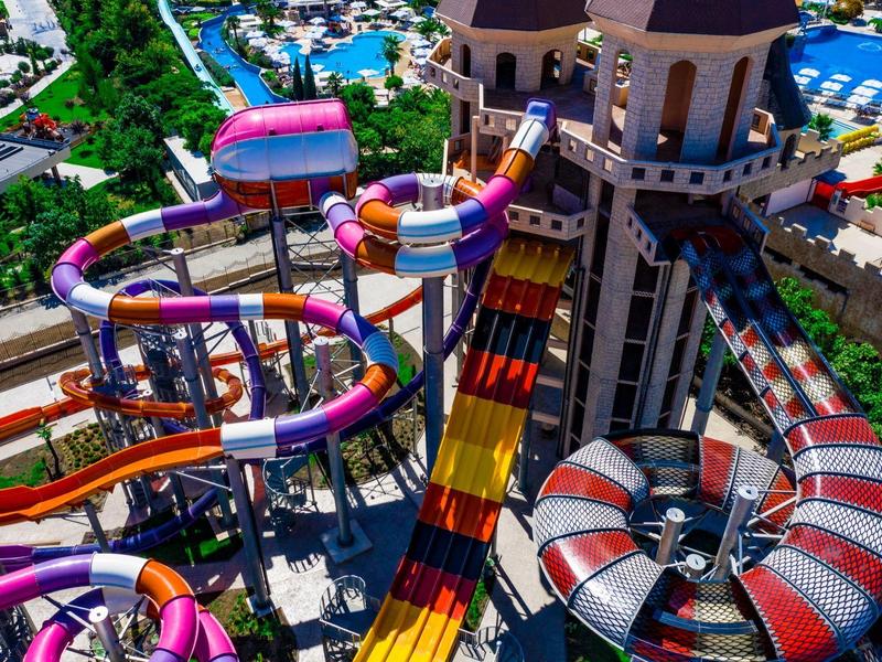 Kleurrijke glijbanen slingeren rond een waterparktoren met weelderig groen op de achtergrond.