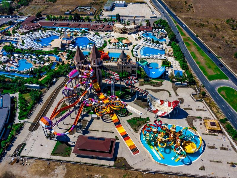 Luchtfoto van een kleurrijk waterpark met glijbanen, zwembaden en droge attracties.