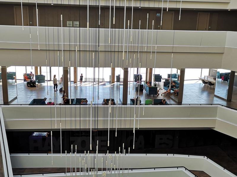 Moderne hotel lobby met zitgedeelte op meerdere niveaus, grote ramen en hangende lampen.