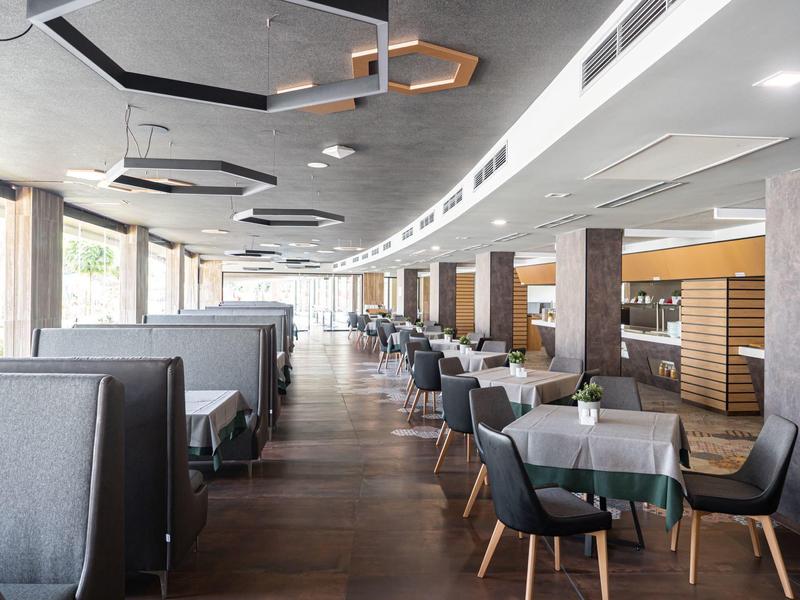 Modern interieur van restaurant met tafels, stoelen, booth-zitplaatsen en geometrische plafondlampen.