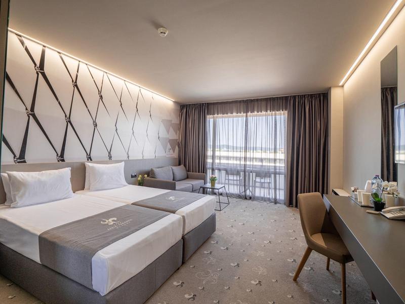 Moderne hotelkamer met twee eenpersoonsbedden, groot raam en werkruimte met stoel.