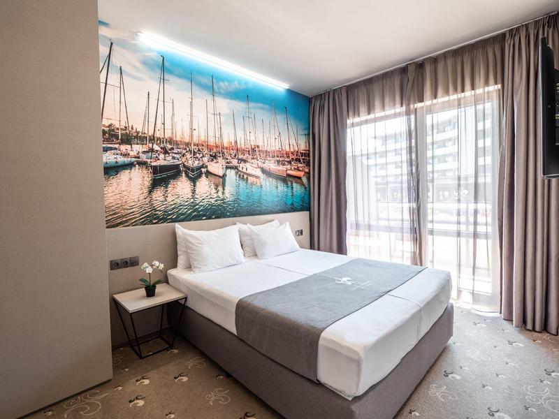 Moderne hotelkamer met groot bed, wanddecoratie van een marina en doorschijnende gordijnen voor balkonraam.