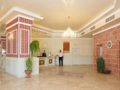 Helle Hotellobby mit Rezeption, Pflanzen und Kronleuchter.