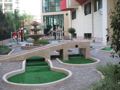 Minigolfplatz mit Brücke und Springbrunnen neben einem Hotelgebäude.