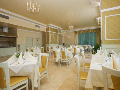 Hell eingerichteter Speisesaal mit gedeckten weißen Tischen und goldgelben Stühlen.