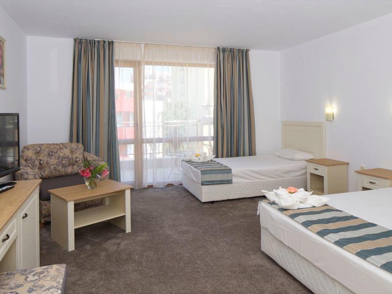 Hotelzimmer mit zwei Einzelbetten, Fernseher, Sitzbereich und Balkon mit Vorhängen.