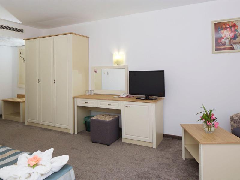 Hotelzimmer mit Schrank, Schreibtisch, Fernseher und Sofa, hell und schlicht eingerichtet.