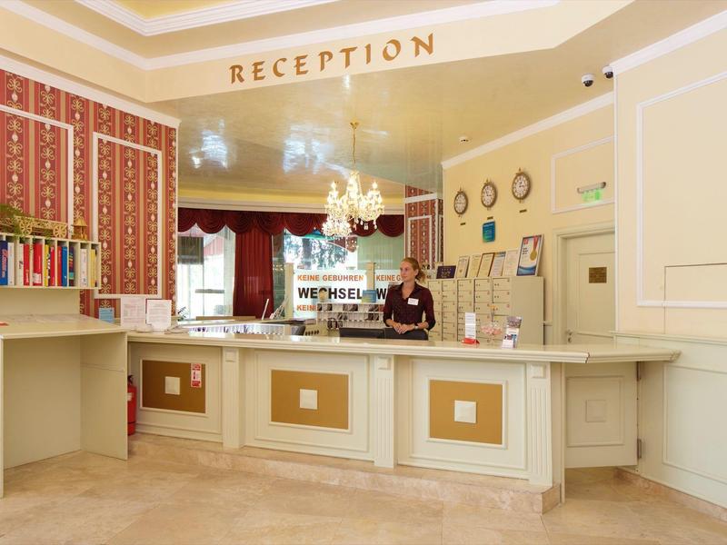 Helle Hotellobby mit Rezeptionstresen und Empfangspersonal in eleganter Umgebung.