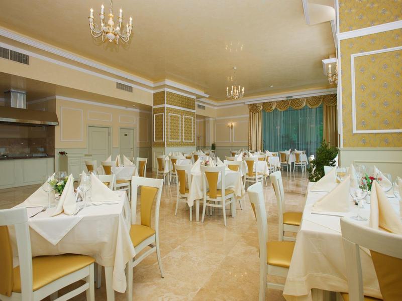 Hell eingerichteter Speisesaal mit gedeckten weißen Tischen und goldgelben Stühlen.