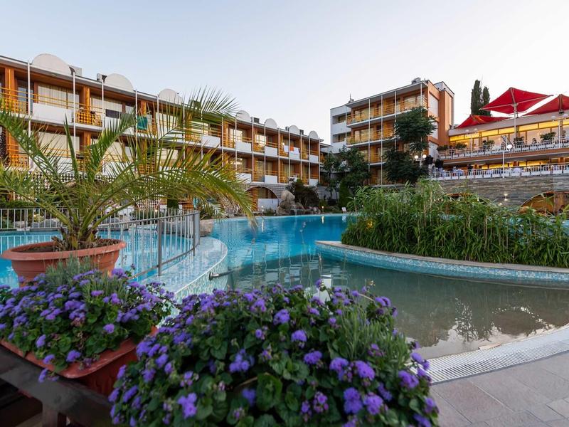 Hotel with multi-story buildings, large pool, and flower beds in the foreground.