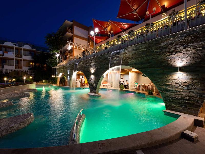 Illuminated pool with waterfalls at a hotel complex at night.