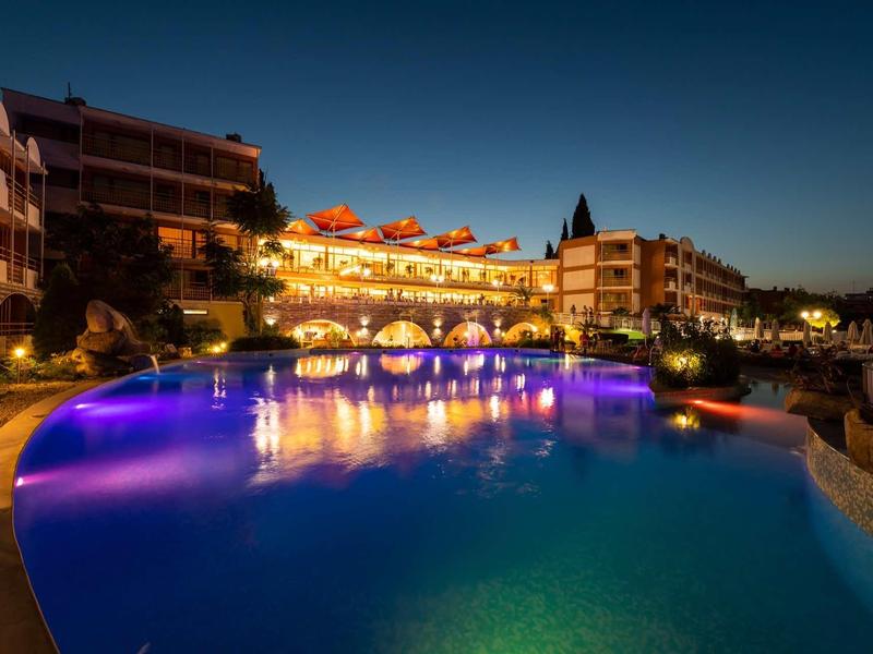 Illuminated pool at night in front of hotel buildings with clear evening ambiance.