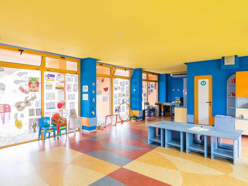 Colorful children's playroom with large windows, chairs, and tables.