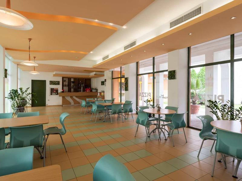 Spacious, bright dining area with green chairs and tables, large windows, and plants.