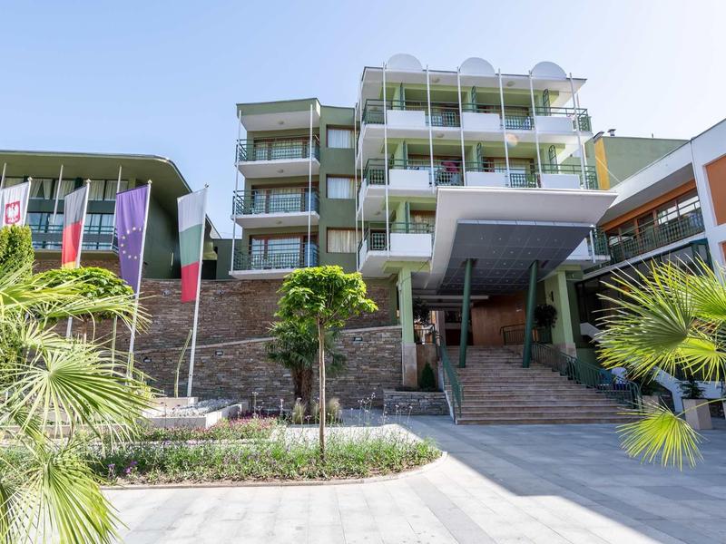 Modern hotel with balconies, palm trees, and clear sky.