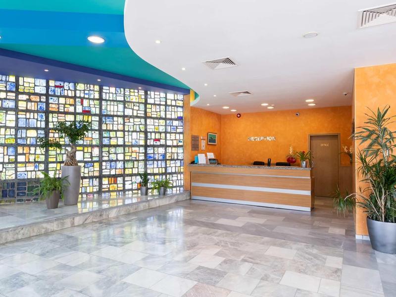 Bright hotel lobby with marble floor, reception desk, and decorative glass wall.