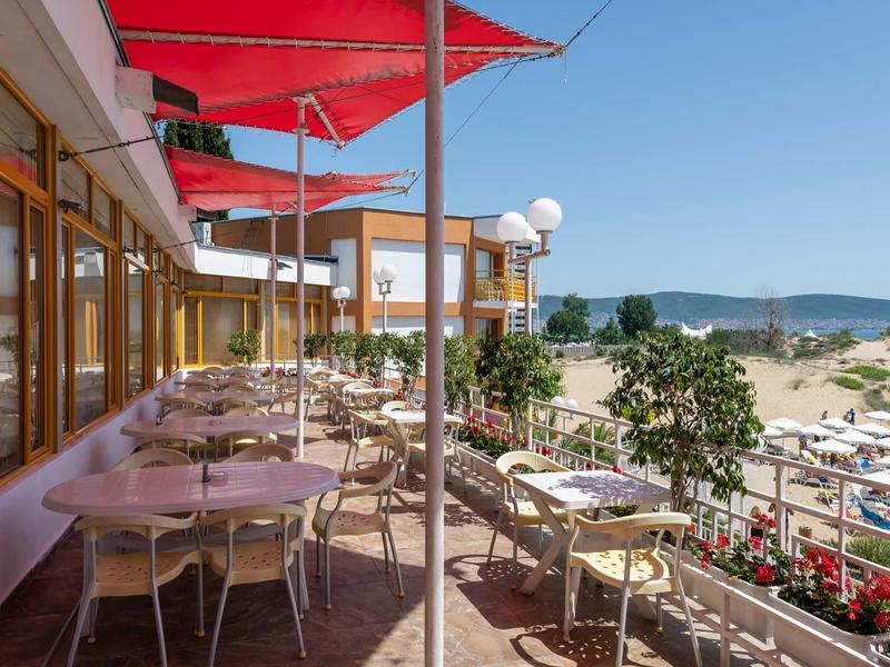 Terrace with tables and chairs, red awnings, and sea view on a sunny day.