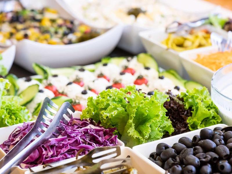 Colorful salad bar with fresh vegetables, olives, and various dressings.