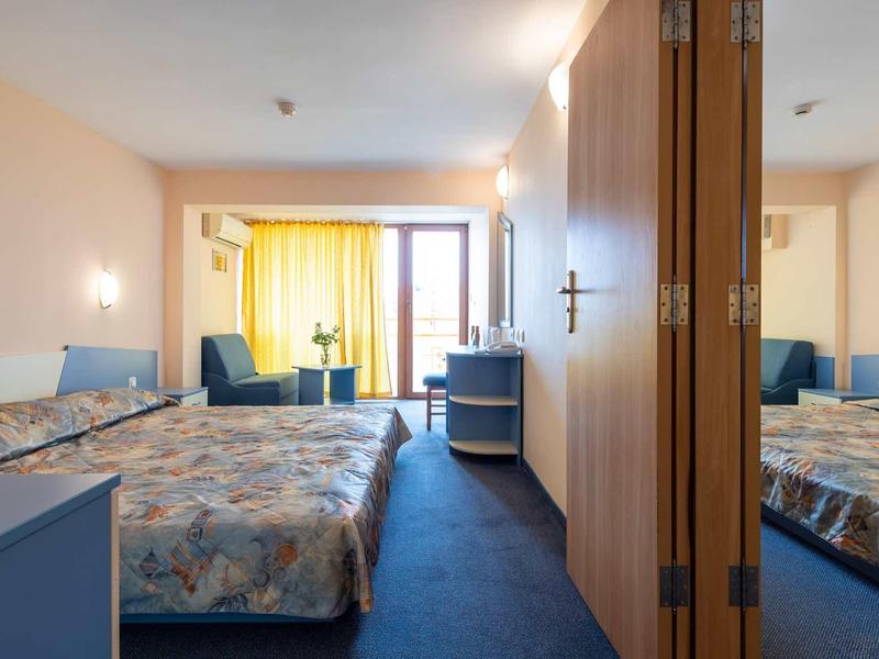 Hotel room with double bed, armchairs, yellow curtains, and mirror.