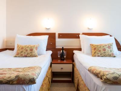 Hell beleuchtetes Hotelzimmer mit zwei Einzelbetten, Nachttisch und Telefon dazwischen.