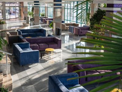 Moderner Hotel-Loungebereich mit blauen und violetten Sofas, Tischen und großen Fenstern.