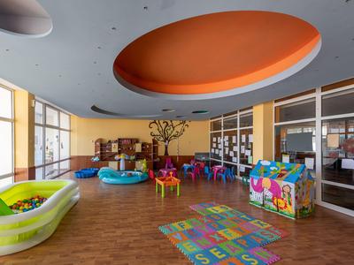 Helles Kinderspielzimmer mit buntem Ballpool, Tischen und großem orangem Deckenelement.