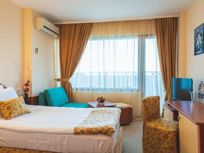 Helles Hotelzimmer mit Einzelbett, großem Fenster, Schreibtisch und Sitzgelegenheit.
