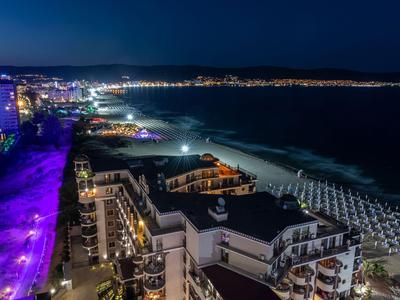 Nächtliche Küstenstadt mit beleuchteten Hotels und leeren Strandliegen entlang der Küste.