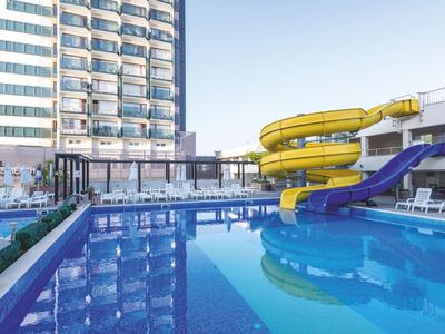 Moderner Hotelpool mit Rutschen neben einem mehrstöckigen Gebäude bei klarem Himmel.