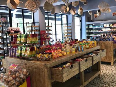 Ein heller Laden mit Holzregalen, bunten Snacks und hängenden Strohhüten an der Decke.