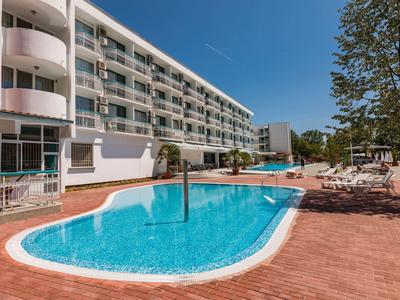 Moderner Hotelkomplex mit blauem Pool, Sonnenliegen und Bäumen unter klarem Himmel.