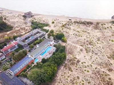 Blick auf ein Hotel mit Pool neben einer ausgedehnten Dünenlandschaft an einem Küstenstrand.