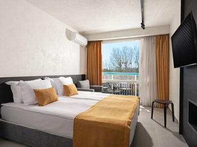 Klares Zimmer mit Doppelbett, weißen Wänden, braunen Vorhängen und Balkon mit Aussicht.