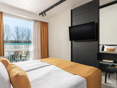 Helles Schlafzimmer mit Doppelbett, braunen Vorhängen und großem Fenster mit Blick ins Freie.