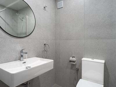 Minimalistisches Badezimmer mit grauen Fliesen, rechteckigem Waschbecken und rundem Spiegel.