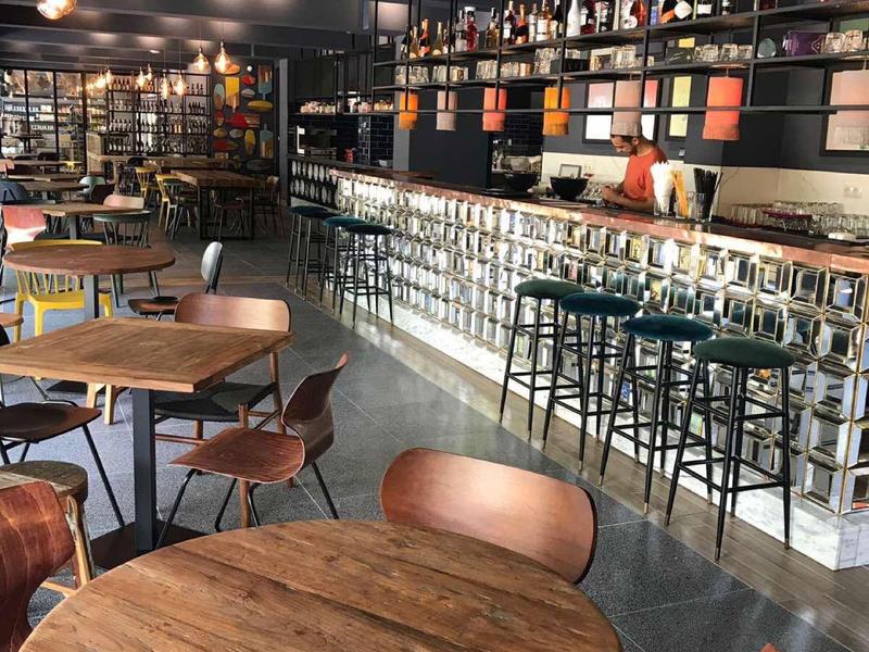 Modernes Café mit runden Holztischen, gemütlichen Stühlen und langer beleuchteter Bar.